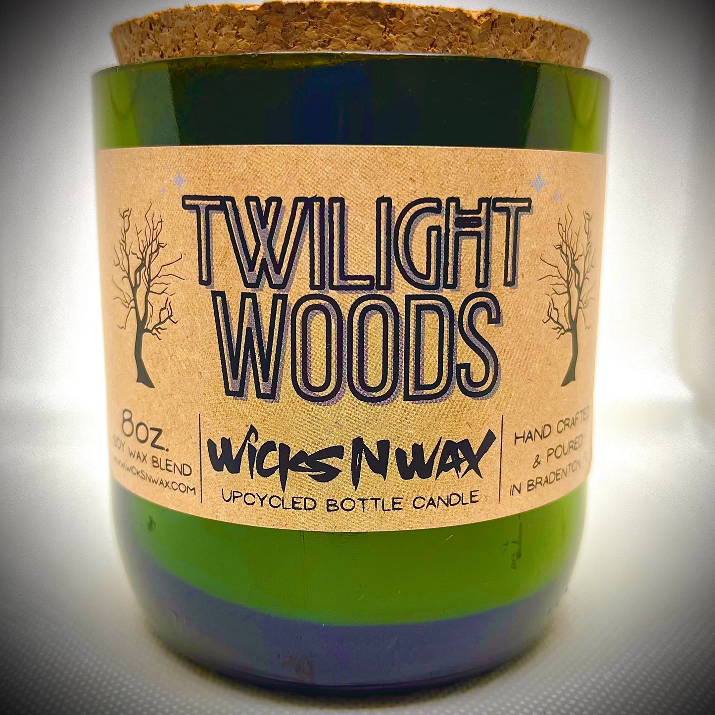 Green glass champagne bottle candle with beige label reading Twilight Woods, WicksNWax.