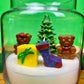 Christmas art candle with a tree, two teddy bears, gift and stockings in white wax