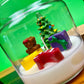Christmas art candle in a tilted clear jar, with white wax and colorful holiday figures