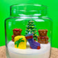 Christmas candle in a glass jar with a tree, teddy bears, gift, and purple stocking embed