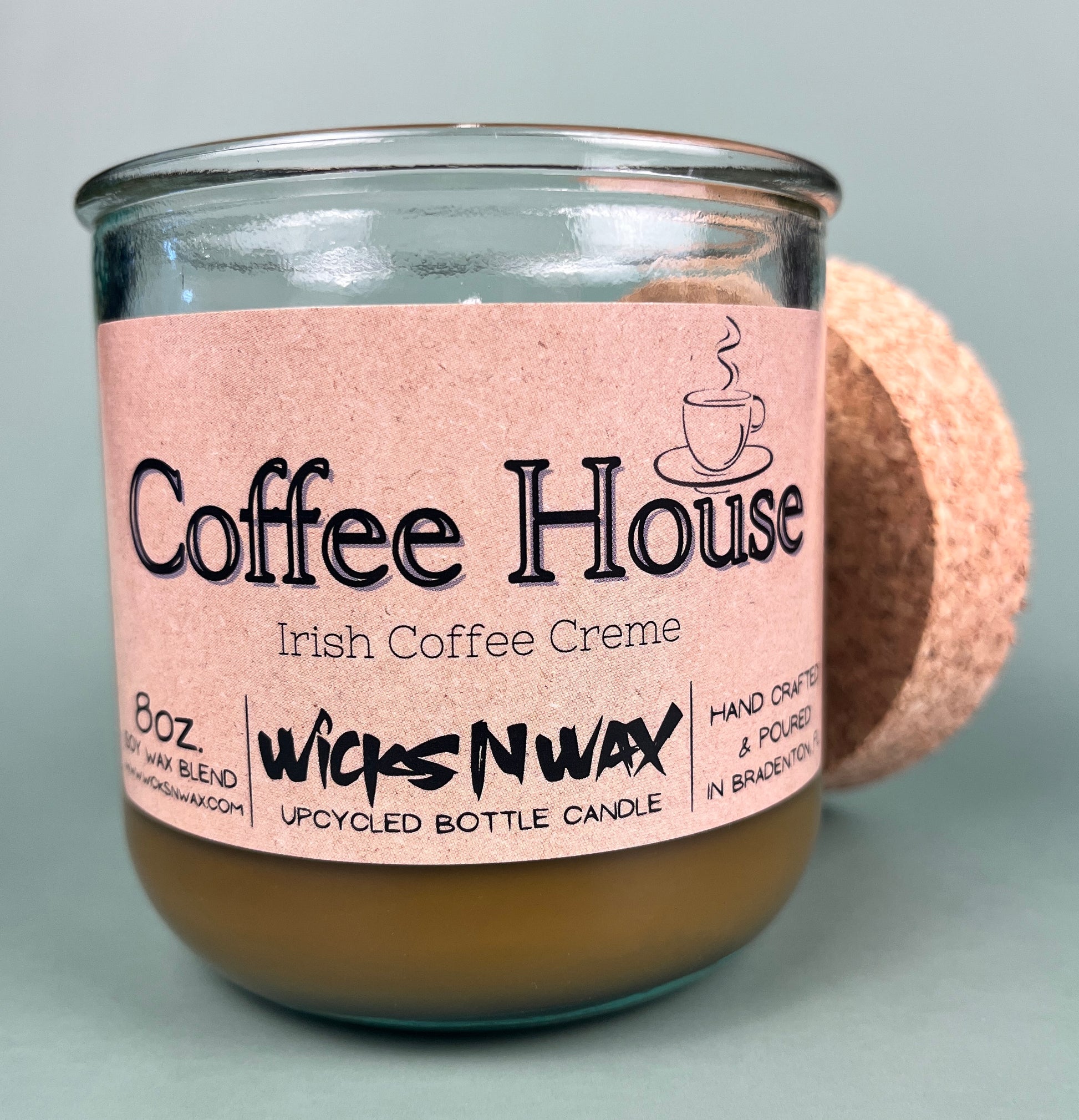 Recycled glass candle, amber wax, pink label facing forward, with cork coaster behind
