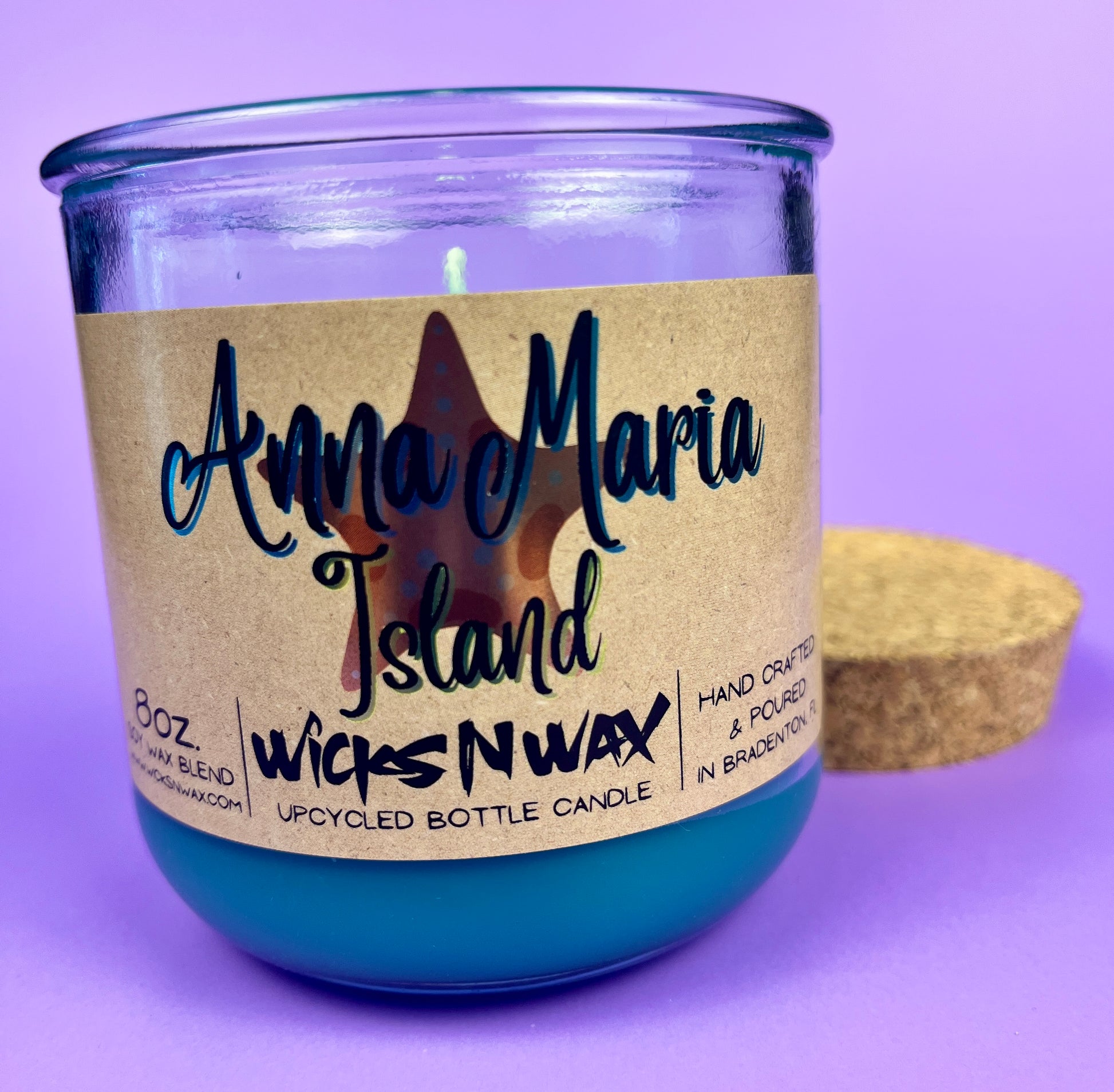Recycled glass bottle candle with blue wax, beige label, and cork lid; visible wick