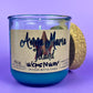 Recycled glass candle with blue wax, beige label, and cork lid leaning behind