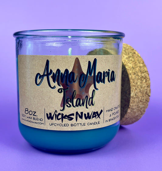 Recycled glass candle with blue wax, beige label, and cork lid leaning behind