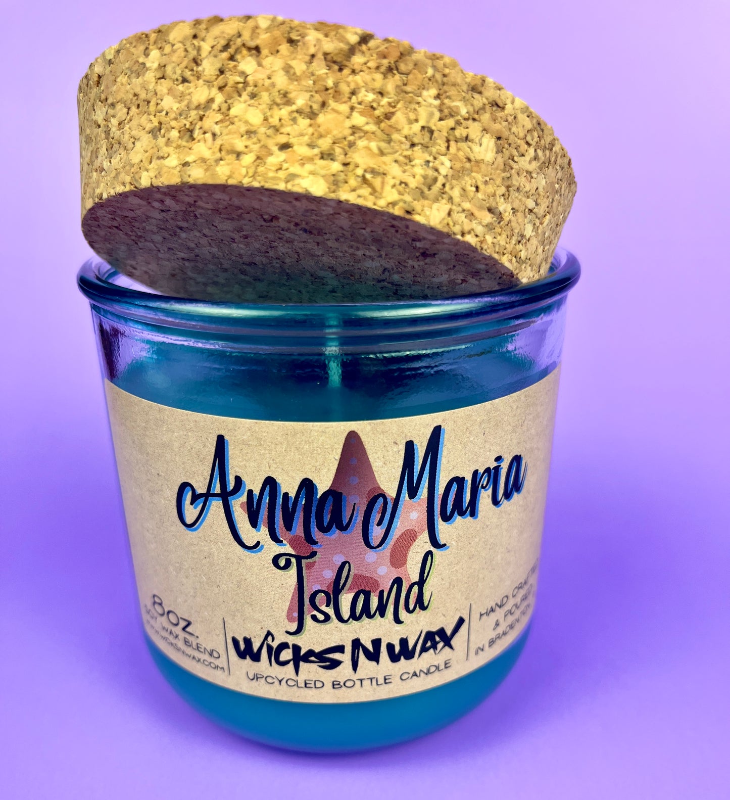 Recycled glass candle with blue wax and beige label, cork lid partly covering top