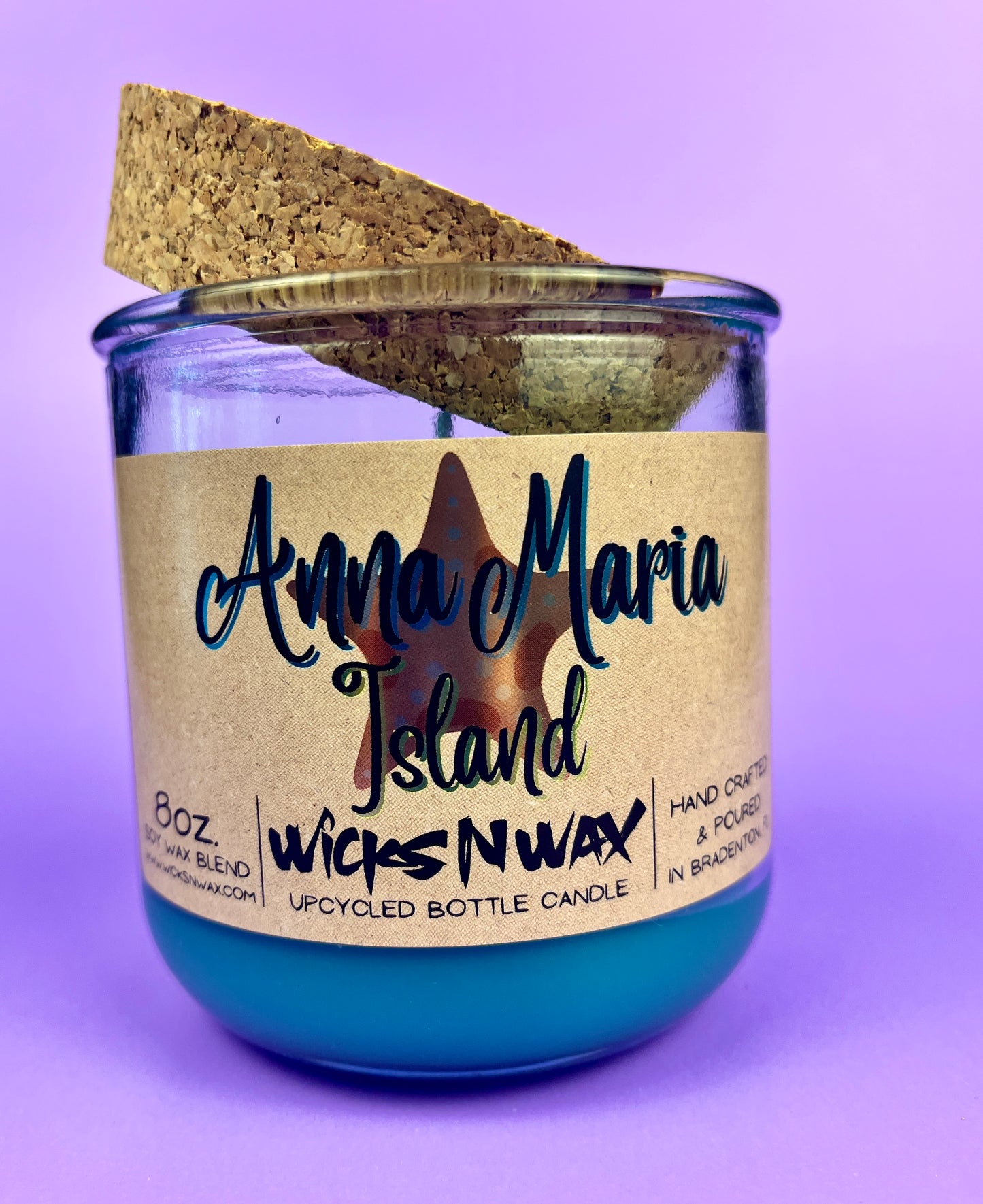 Recycled glass candle with blue wax, beige label, and cork lid tilted behind