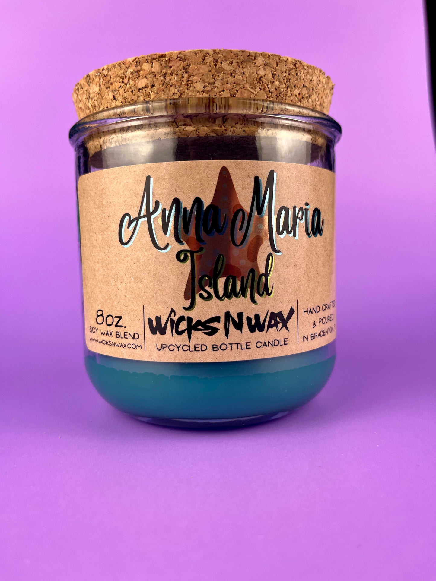 Recycled glass bottle candle with blue wax, beige label, and cork lid on top