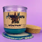 Recycled glass bottle candle with blue wax, beige label, and cork lid resting nearby