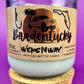 Recycled glass candle in clear jar with white wax and beige label on cork base.