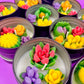 Small candle tin with green leaves, purple flowers, yellow accents, and pink rose