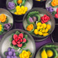 Small candle tin with red rose, green leaves, yellow buds, and purple flower wax