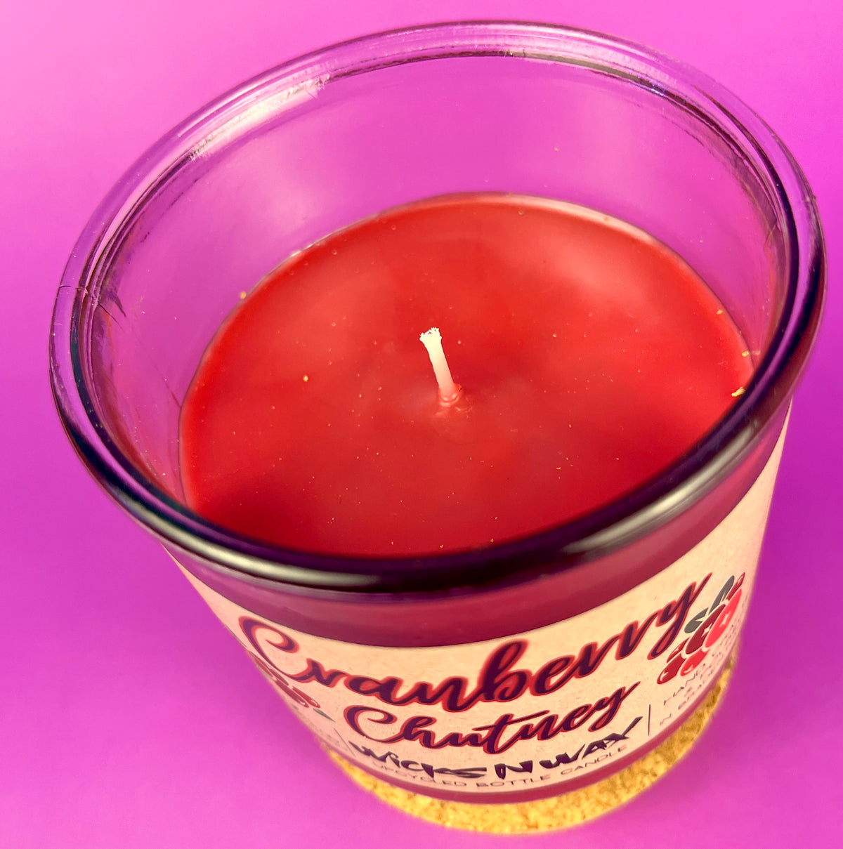 Recycled glass bottle candle with clear rim and magenta wax, lit wick visible