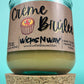 Recycled glass candle with creamy wax on cork base; kraft label shows WicksNWax and Creme Brûlée