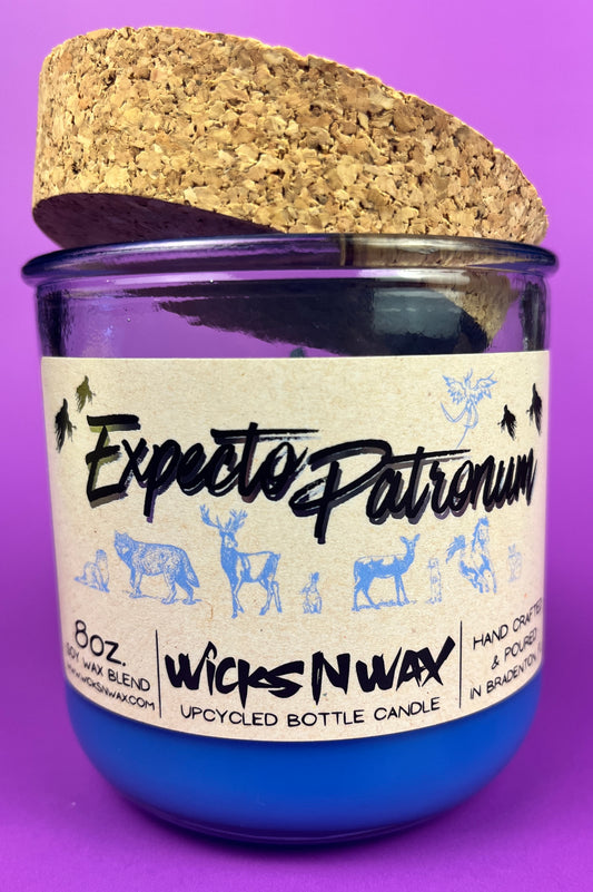 Blue glass candle jar with cream label, cork lid behind it, and illustrated figures