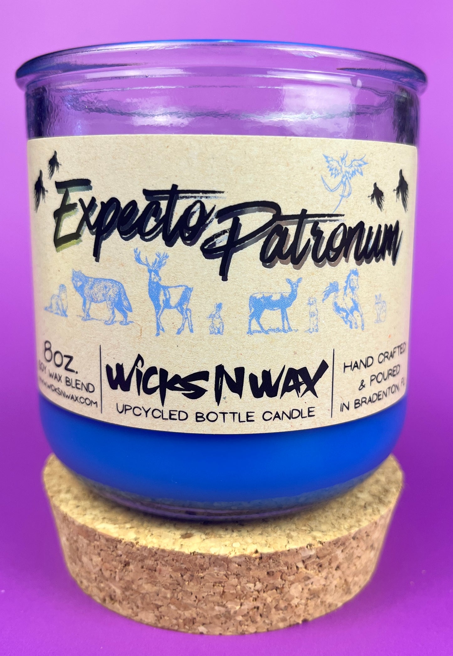 Blue glass candle jar with cream label and illustrated figures, cork base ring shown