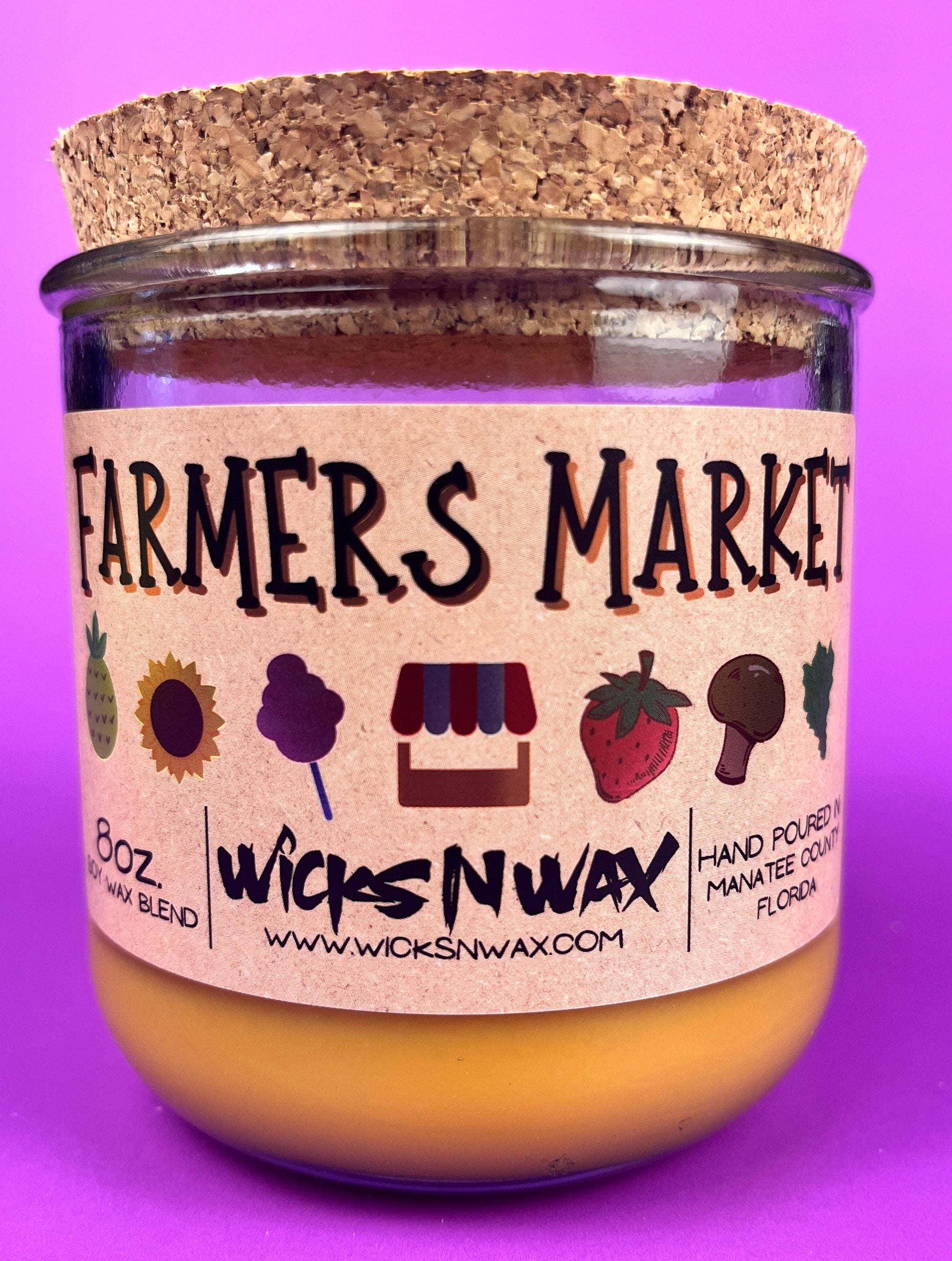 Glass candle jar showing Farmers Market label and amber wax fill, cork lid on top