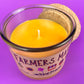 Glass candle cup with amber wax and wick, cork lid behind, Farmers Market label