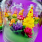 Garden gnome art candle in clear jar with green wax base and multicolor flower and gnome figurines