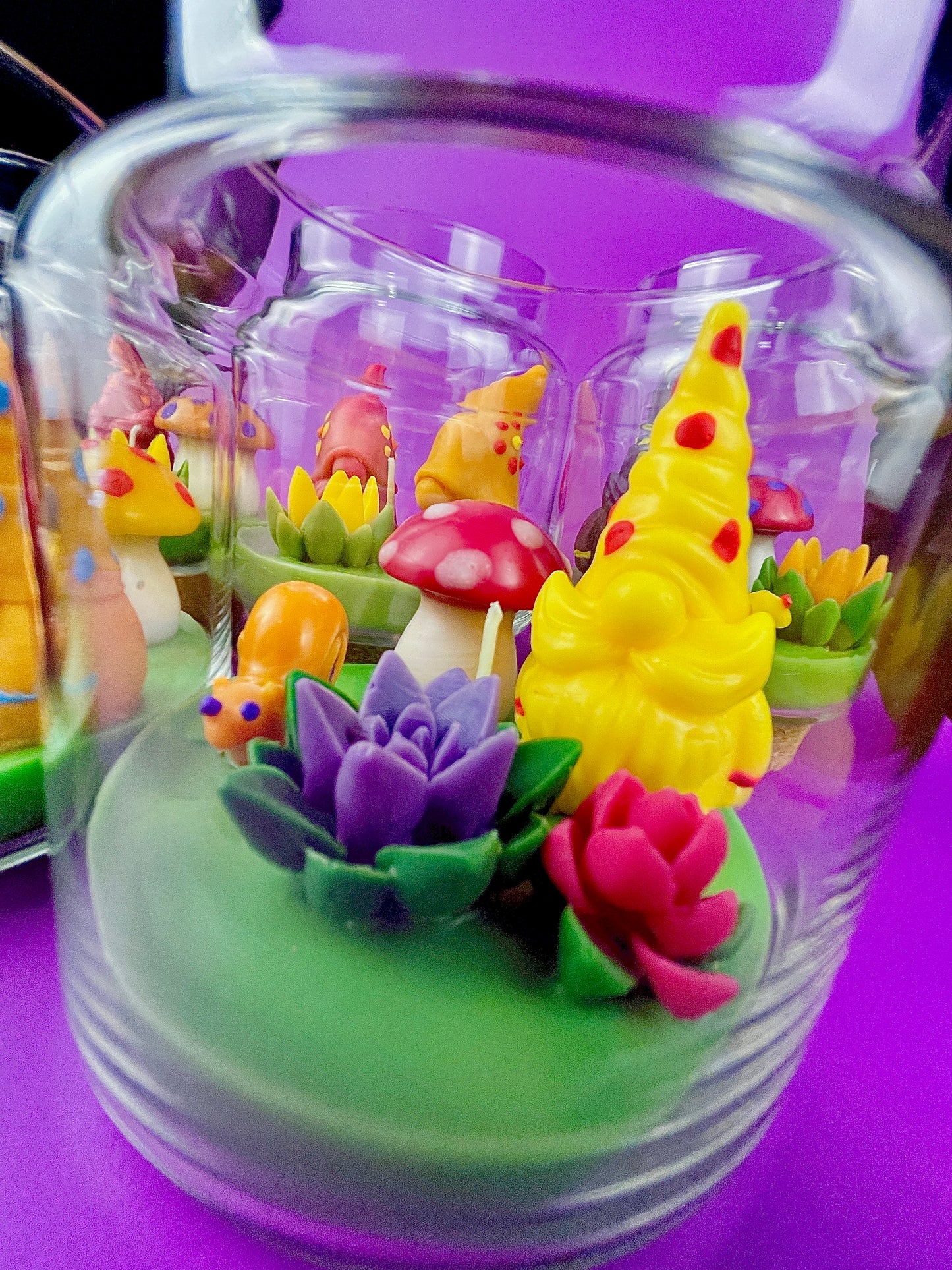 Garden gnome art candle in clear jar with green wax base and multicolor flower and gnome figurines