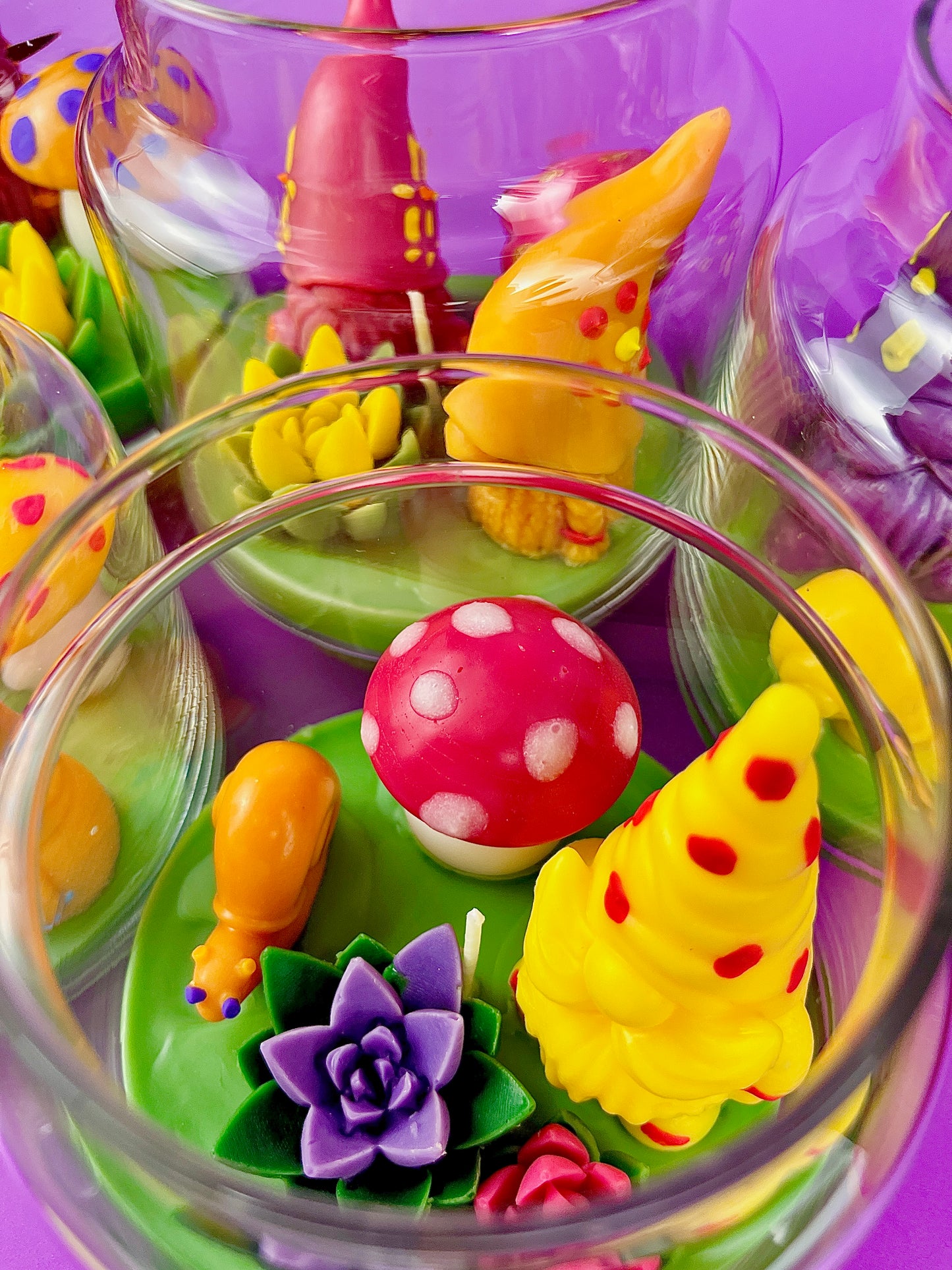 Garden gnome art candle jar with green wax base and purple flowers, red dots, and yellow shapes
