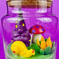 Garden gnome art candle in clear glass jar with purple gnome, blue mushroom, and flower figurines
