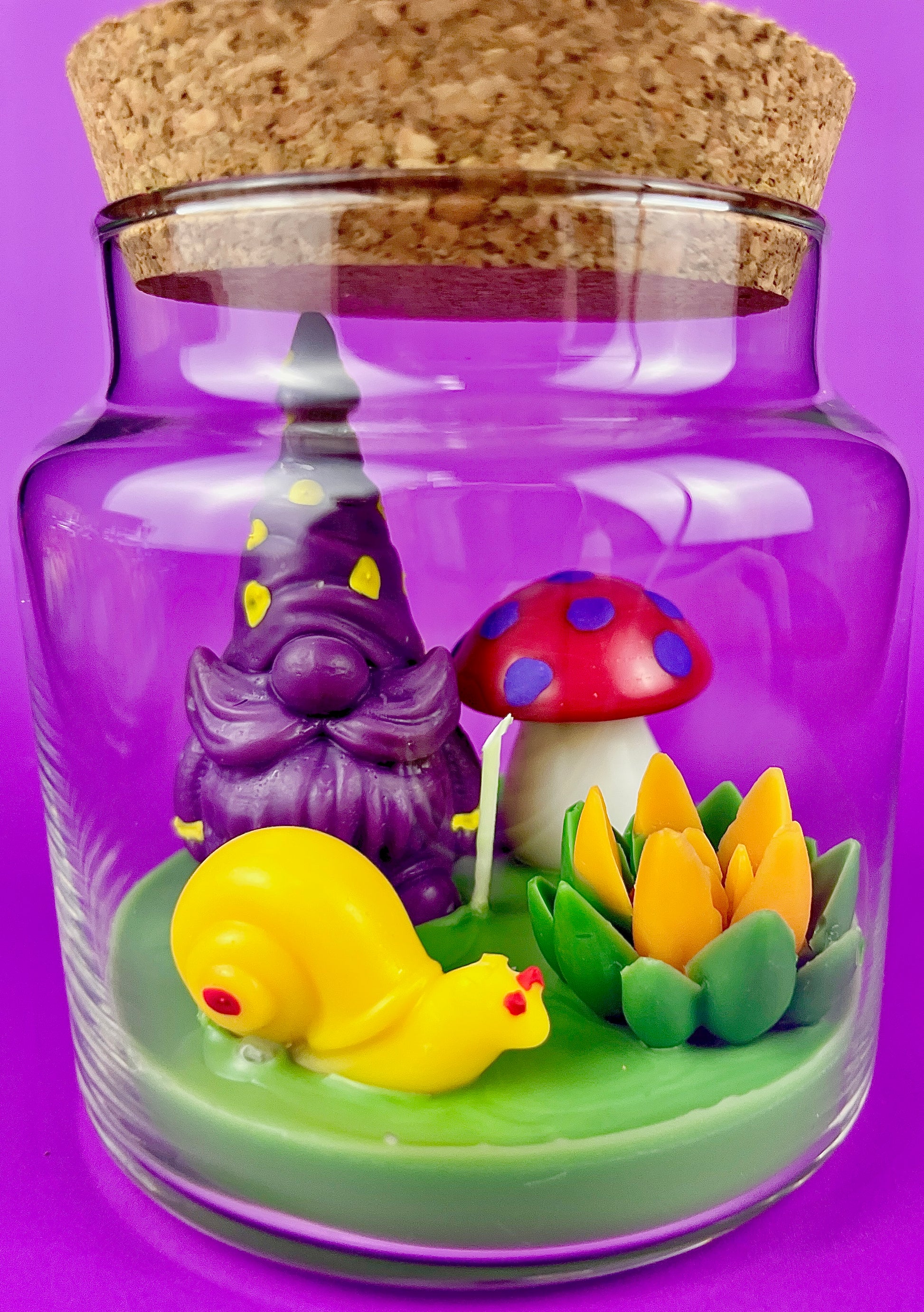 Garden gnome art candle in clear glass jar with purple gnome, blue mushroom, and flower figurines