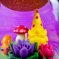 Garden gnome art candle in clear glass jar with yellow gnome, red mushroom, and flower cluster