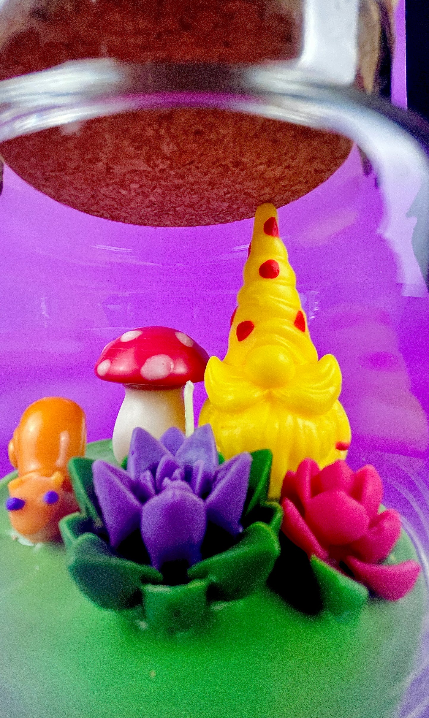 Garden gnome art candle in clear glass jar with yellow gnome, red mushroom, and flower cluster