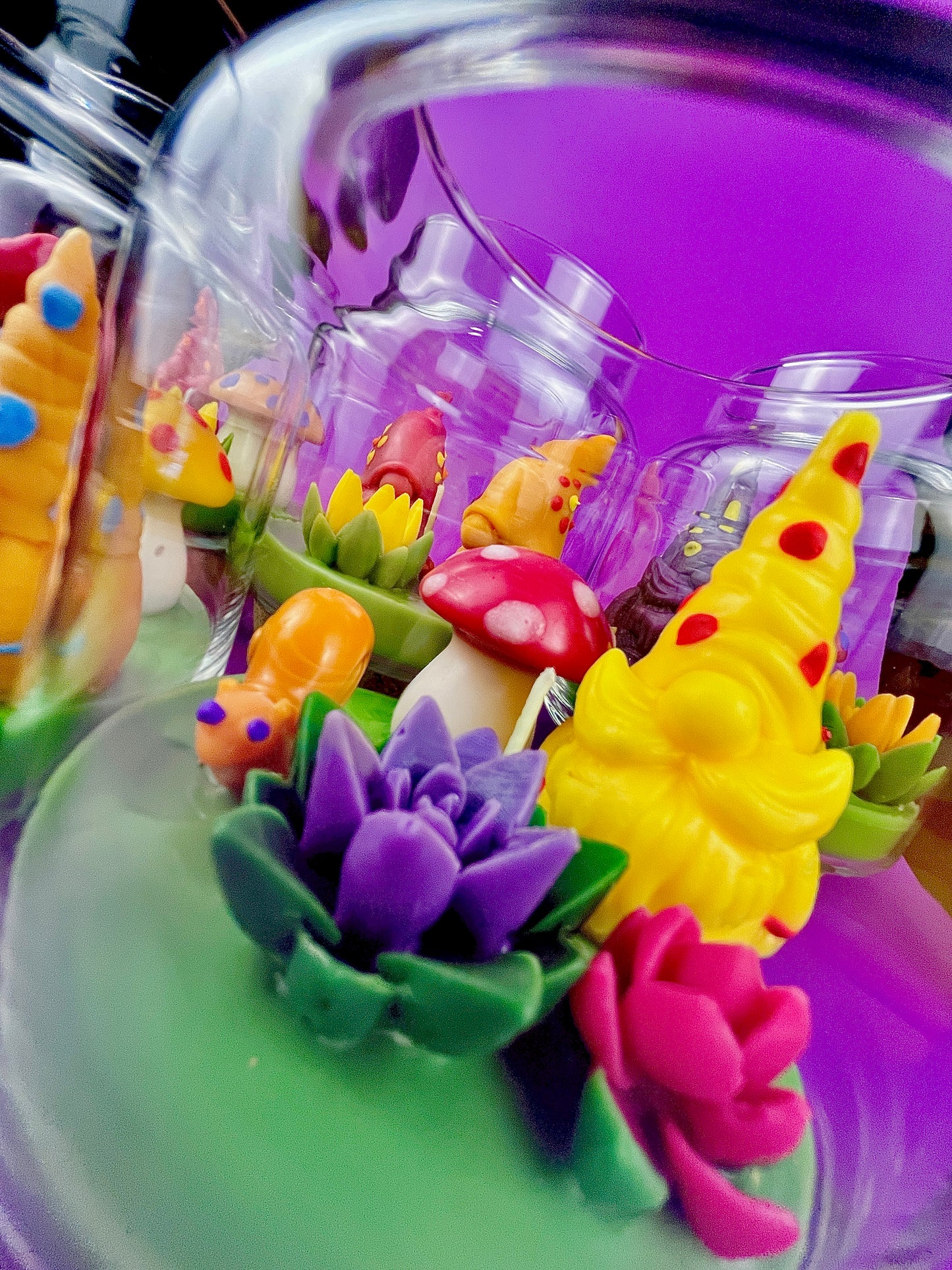 Garden gnome art candle in clear glass jar with green wax and yellow gnome and purple flower shapes