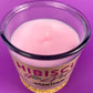 Pink wax candle with wick in purple glass jar, Hibiscus label on cork base