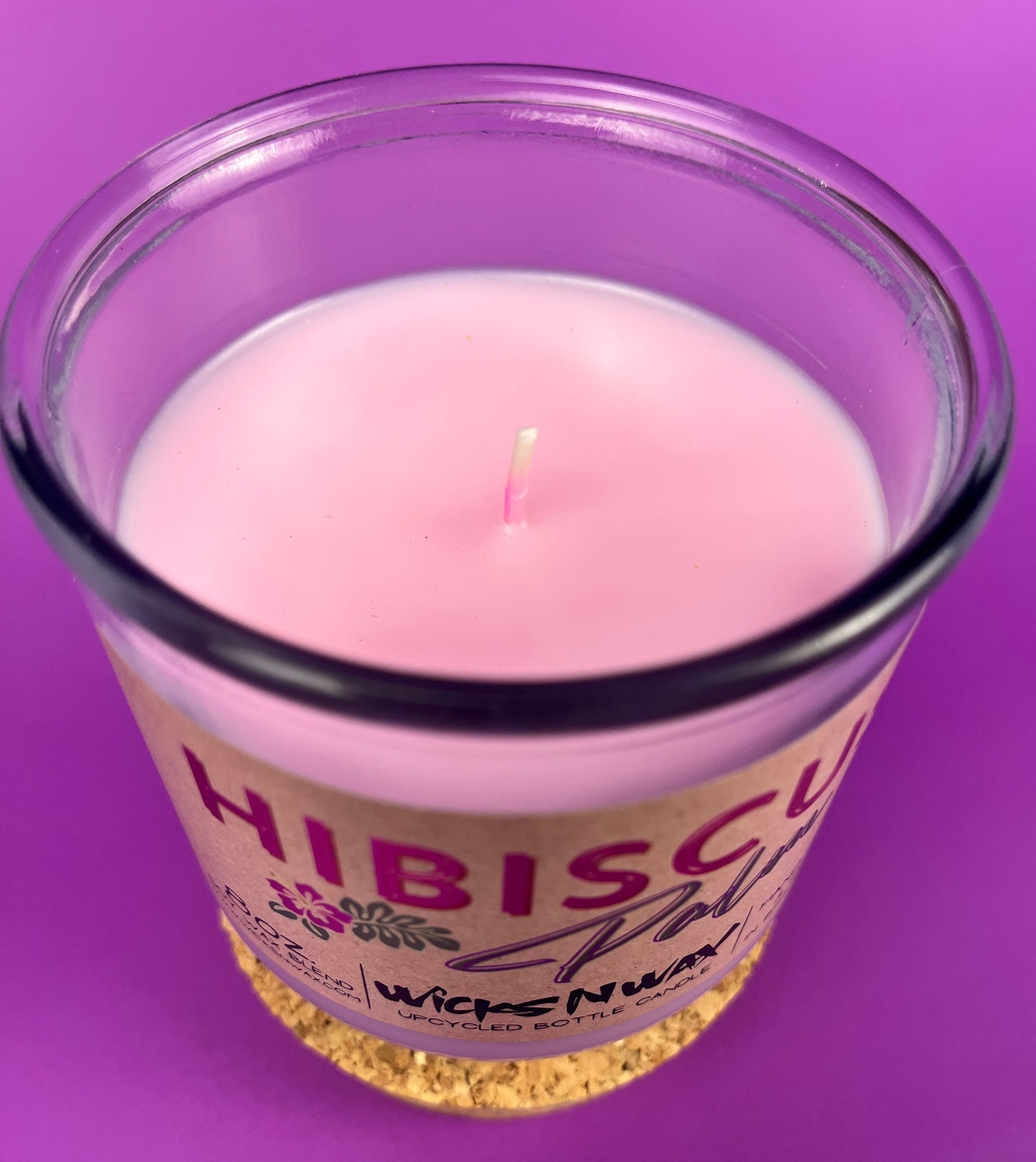 Pink wax candle with wick in purple glass jar, Hibiscus label on cork base