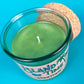 Recycled glass bottle candle with green wax and visible wick, clear glass with cork lid.