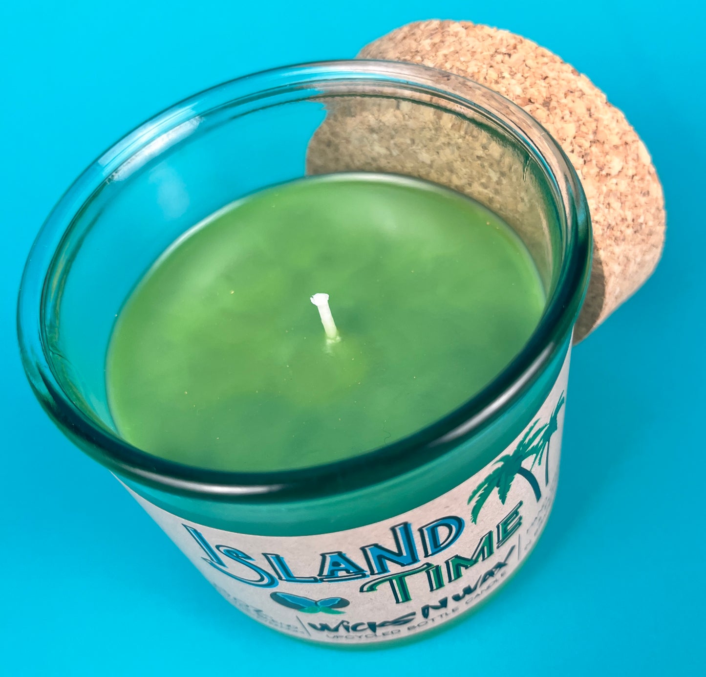 Recycled glass bottle candle with green wax and visible wick, clear glass with cork lid.