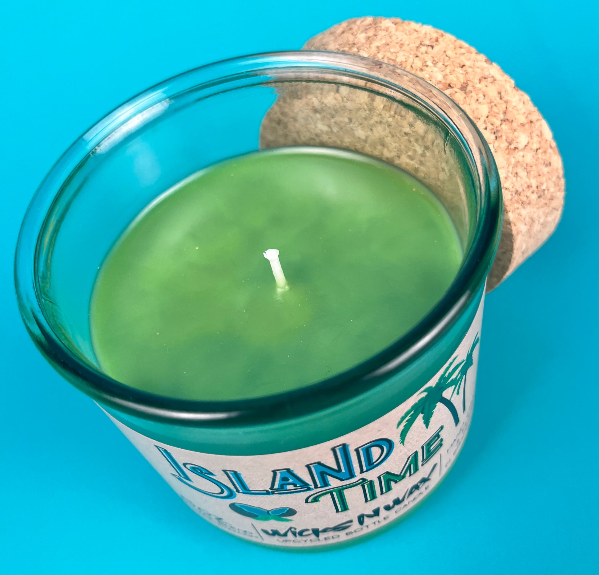 Recycled glass bottle candle with green wax and visible wick, clear glass with cork lid.