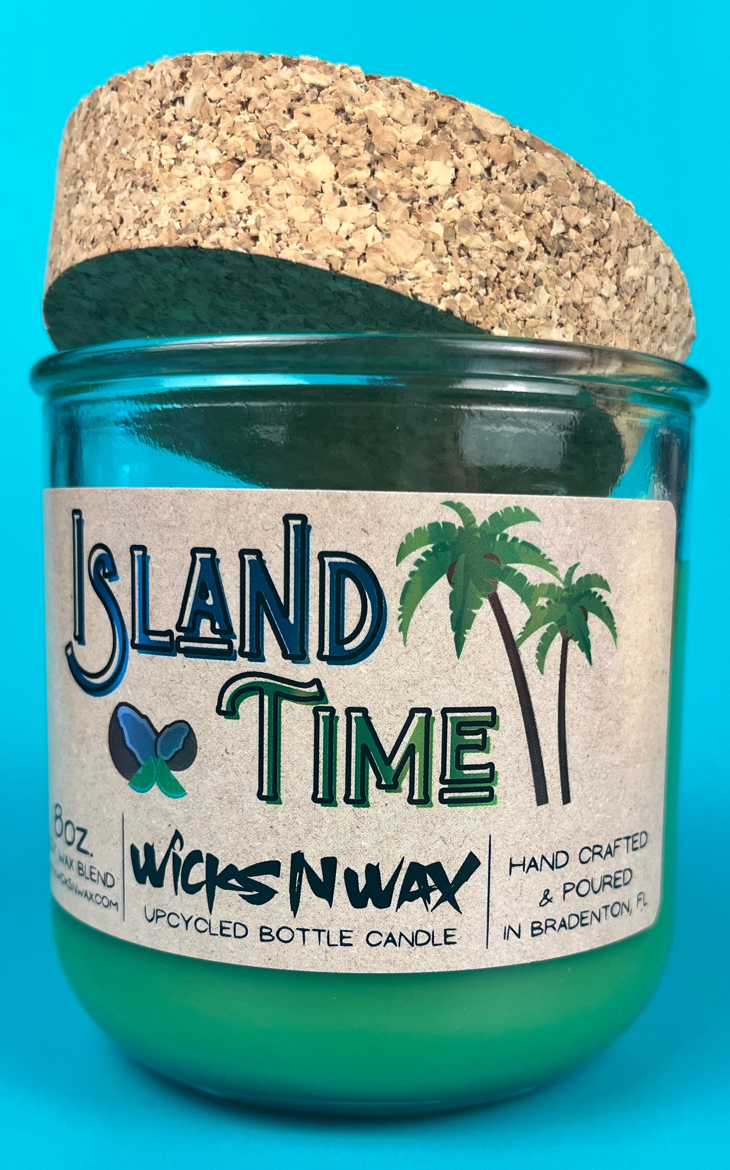 Recycled glass bottle candle with green wax and cork lid, label facing camera in teal glass.
