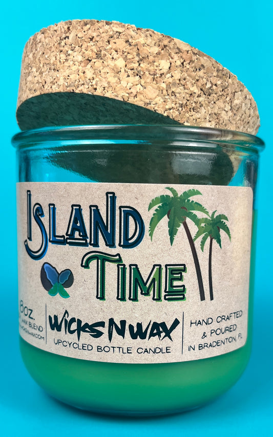 Recycled glass bottle candle with green wax and cork lid, label facing camera in teal glass.