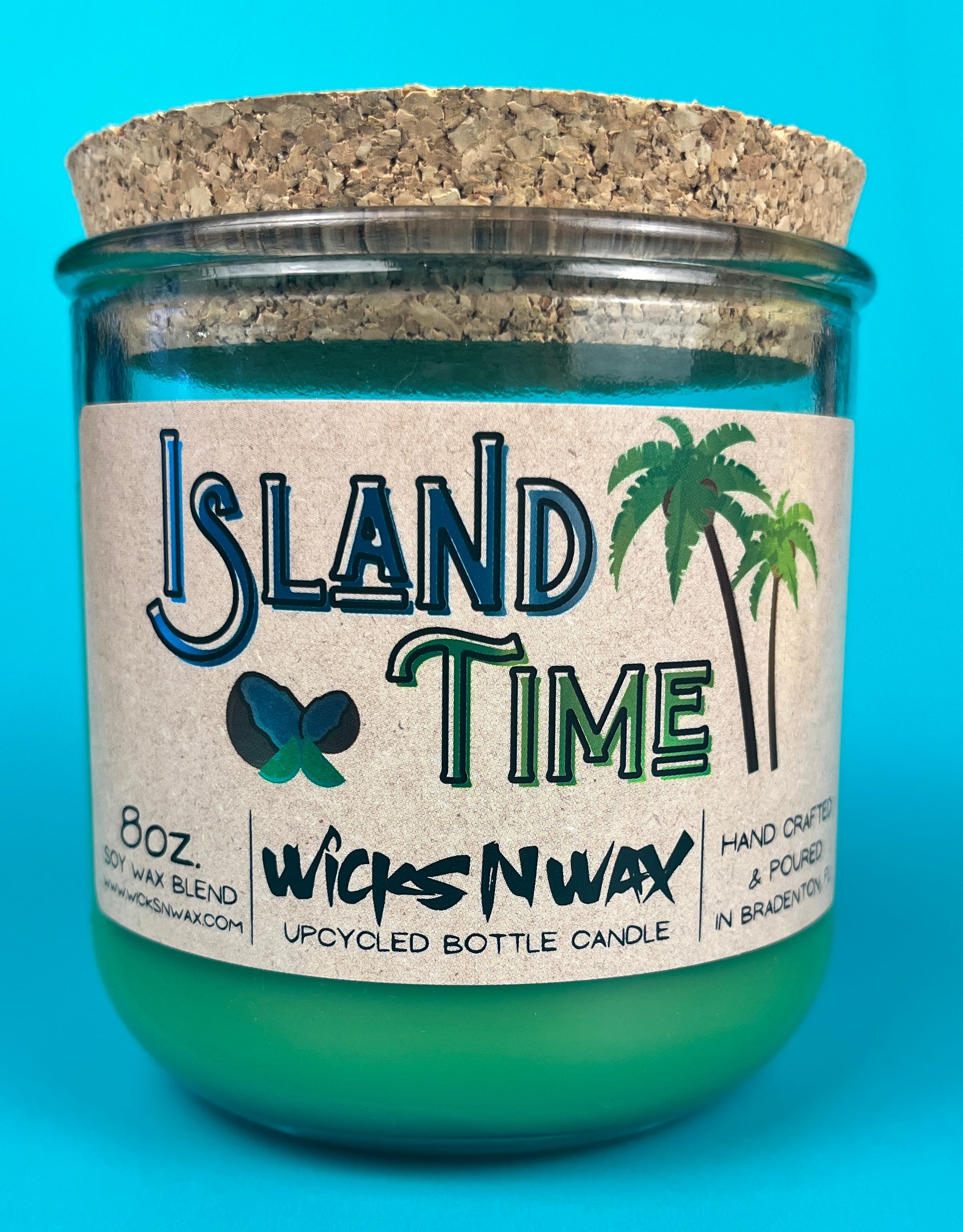 Recycled glass bottle candle with green wax and cork lid, teal glass jar with front branding.
