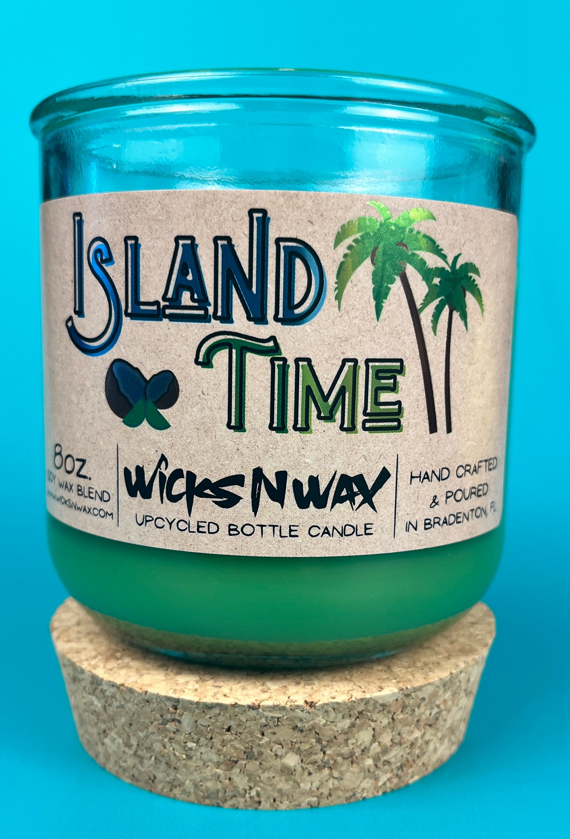 Recycled glass bottle candle with green wax and cork base ring, teal glass and label.