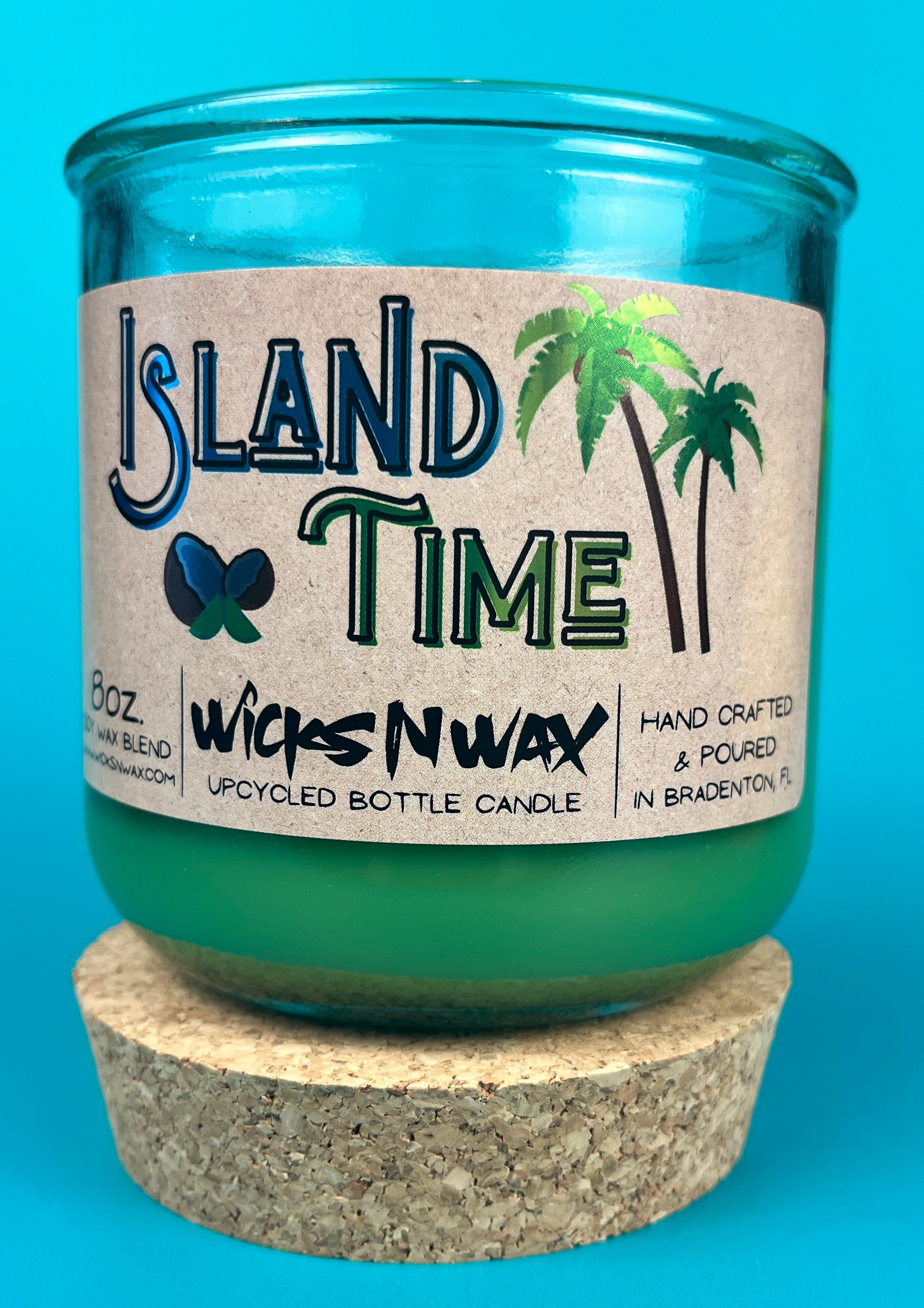 Recycled glass bottle candle with green wax and cork base, teal glass jar with label front.