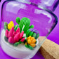 Large cactus art candle in glass jar with tall green cactus and pink, yellow, and purple flowers