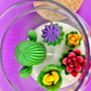 Large cactus art candle close-up in glass jar with green cactus, purple flower, and red rose waxes