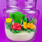 Cactus art candle in clear jar with cork lid; white wax with green cactus and red flowers
