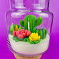 Cactus art candle in clear jar with cork base; white wax with green cactus and red petals