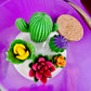 Large cactus art candle close-up in glass jar with green cactus and purple flower waxes