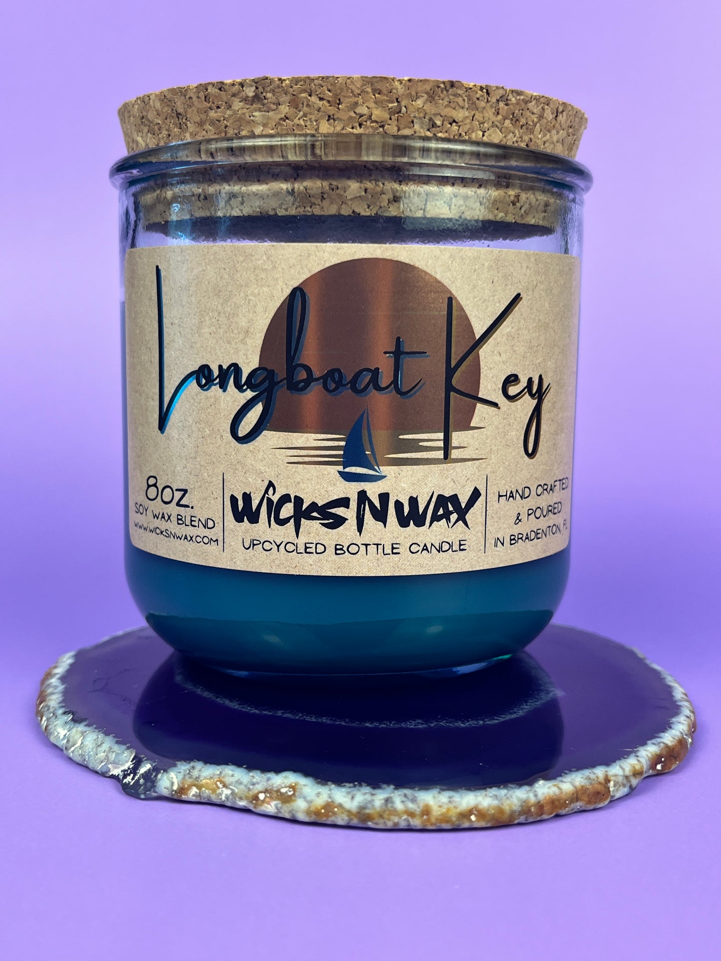 Recycled glass candle in blue wax with cork lid on top, on coaster, label centered