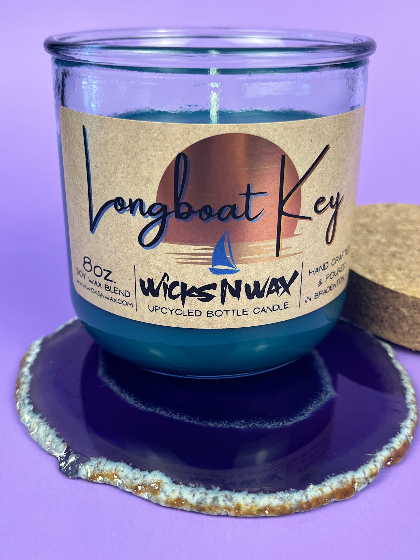 Recycled glass candle in blue wax, on glittery coaster, cork lid behind jar