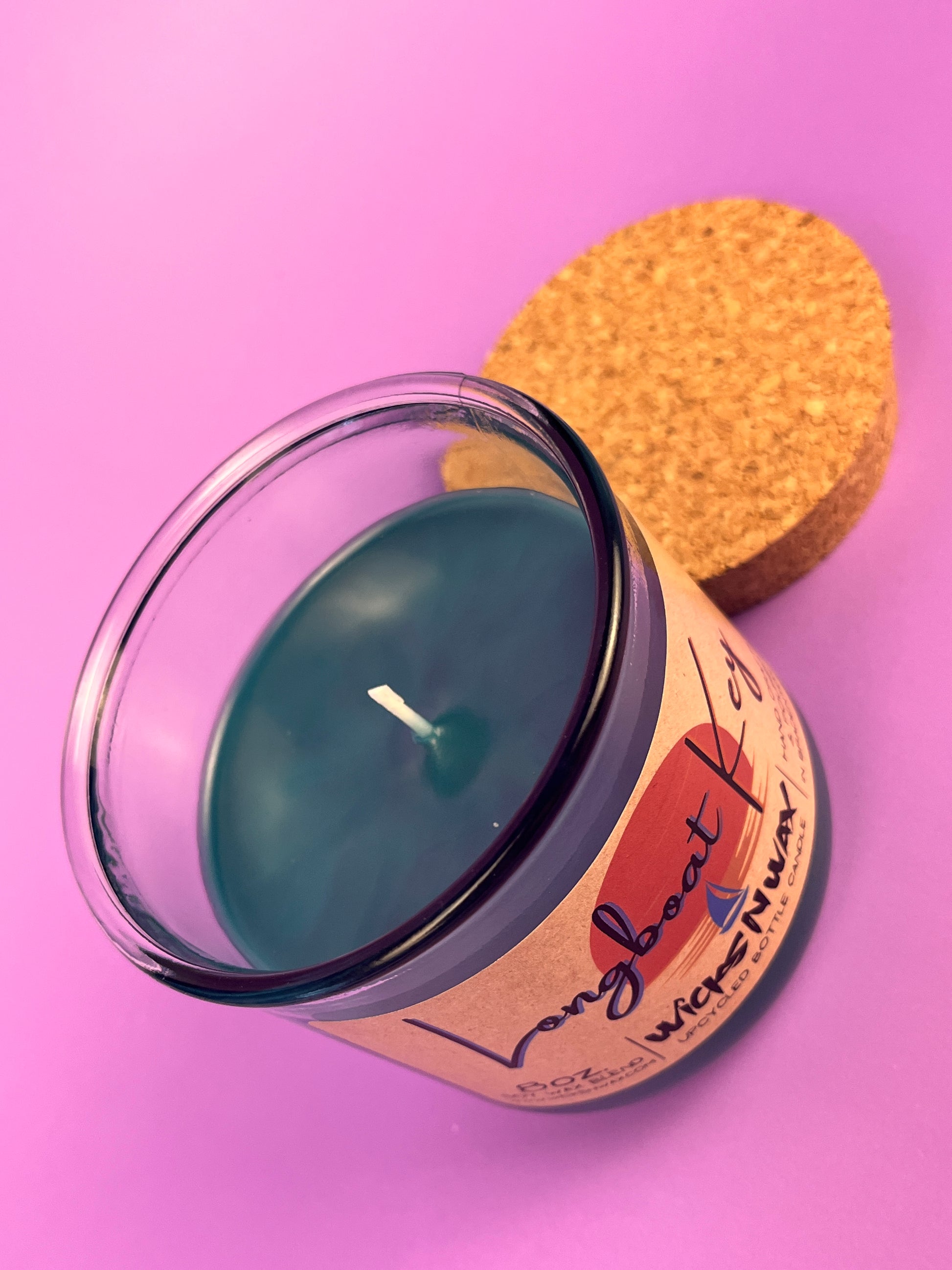 Recycled glass candle with blue wax, cork lid on side, label partly visible