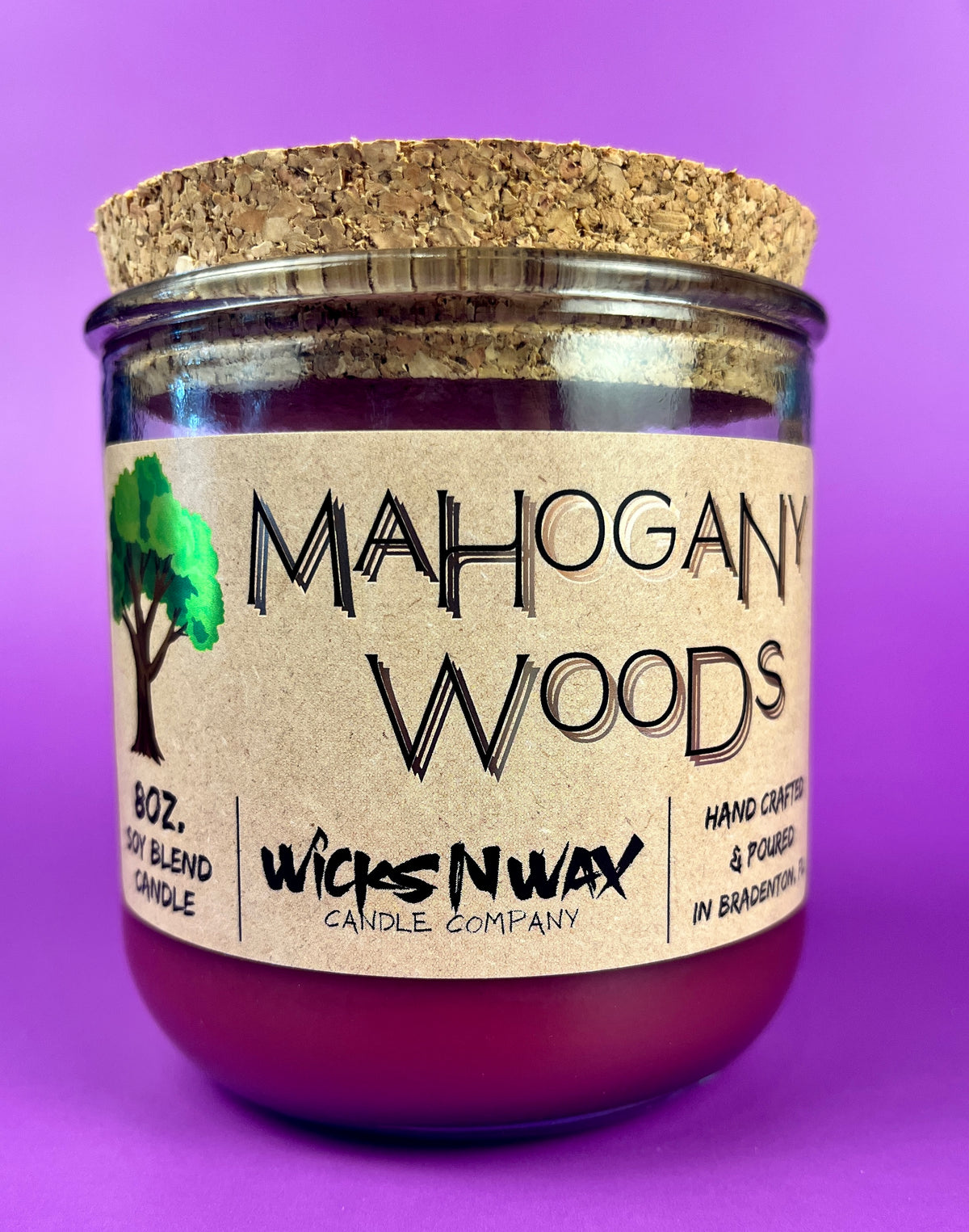 Recycled glass candle with cork lid and purple wax, front label showing Mahogany Woods.