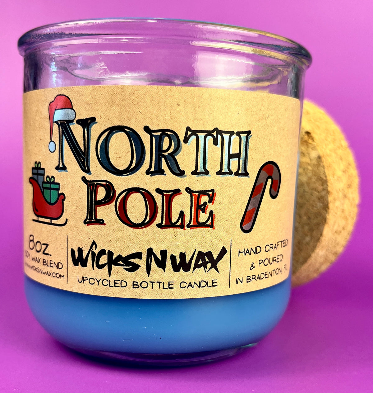 Recycled bottle candle with blue wax and kraft label on purple-tinted glass jar