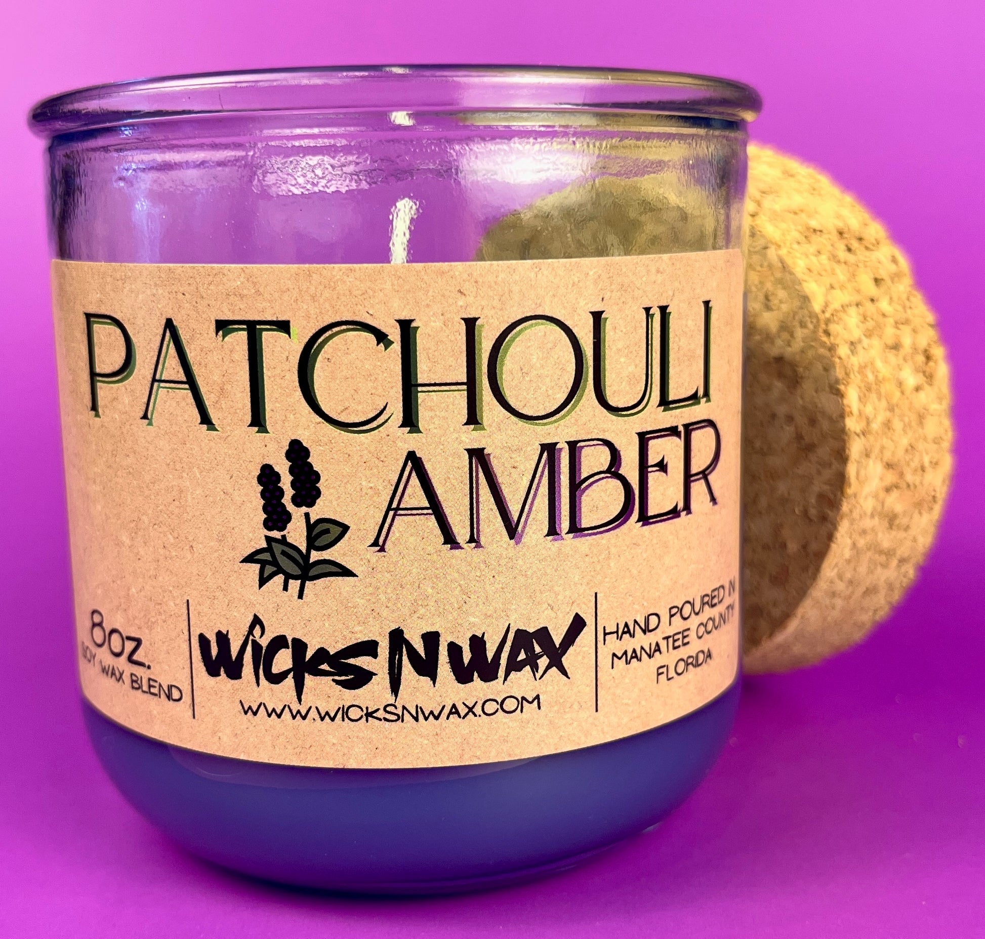 Recycled glass candle label on clear jar with purple wax, cork lid behind.